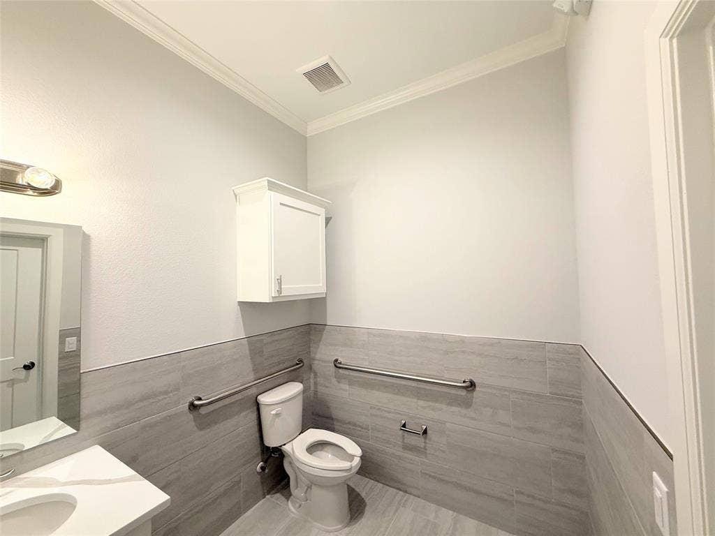 2120 Prairie Drive, #901, Prosper, TX 75078 Crown molding, ceramic tile wainscoting, white wall-mounted cabinet, built-in toilet, and polished chrome grab bars