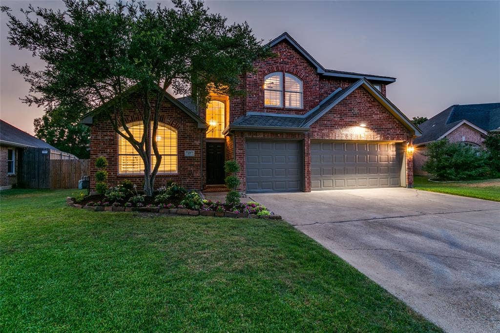 17 Adams Court, Mansfield, TX 76063 Brick exterior with arched windows, attached three-car garage, concrete driveway, and established landscaping