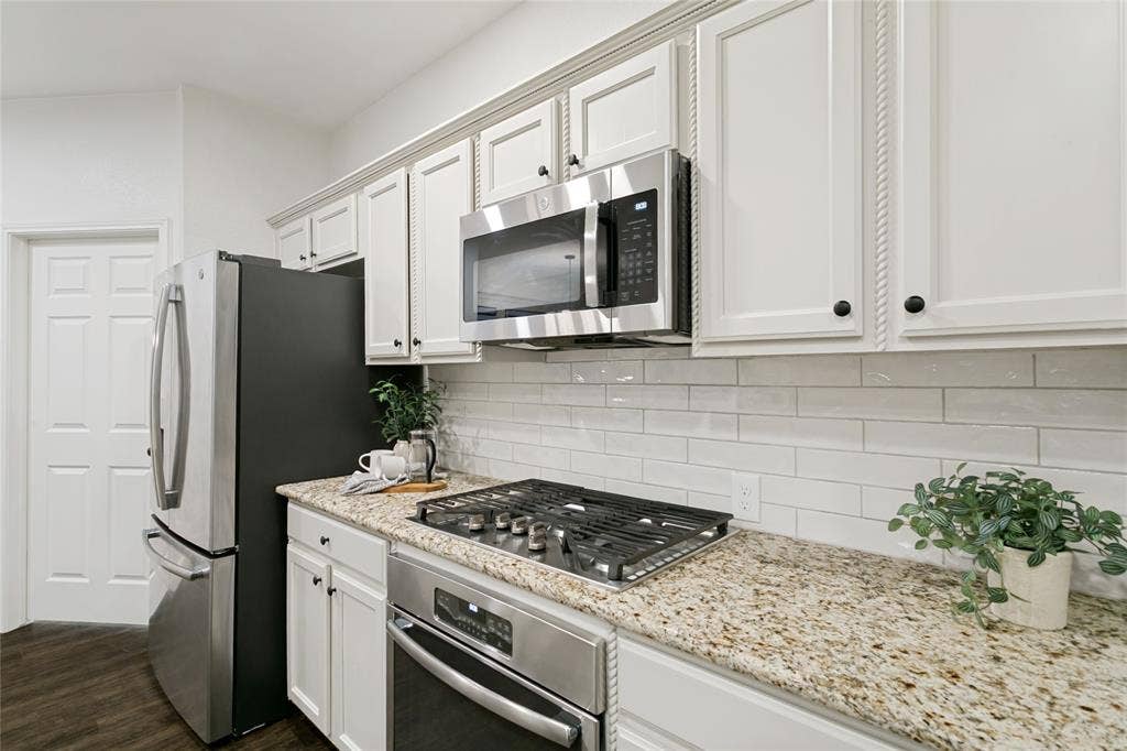 17 Adams Court, Mansfield, TX 76063 White cabinetry with rope trim accents, stainless steel appliances, speckled stone countertops, and a white pearl finish subway tile backsplash