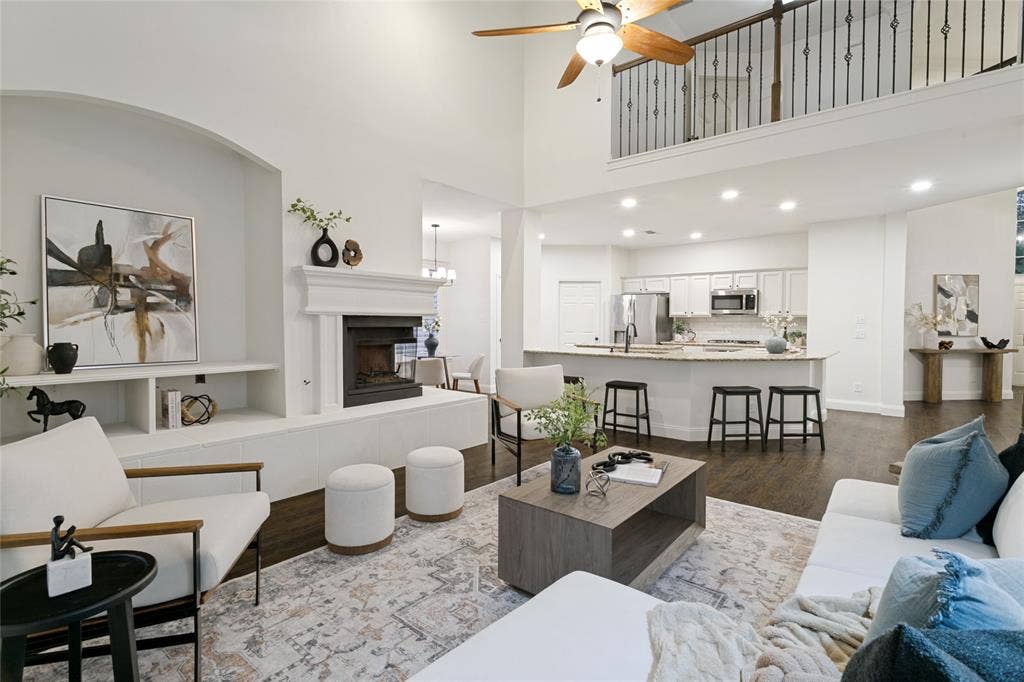 17 Adams Court, Mansfield, TX 76063 Soaring ceilings, a built-in fireplace, dark wood-finish flooring, a kitchen island with seating, and a second-story interior loft overlooking both the front foyer and open concept living features wrought iron railing