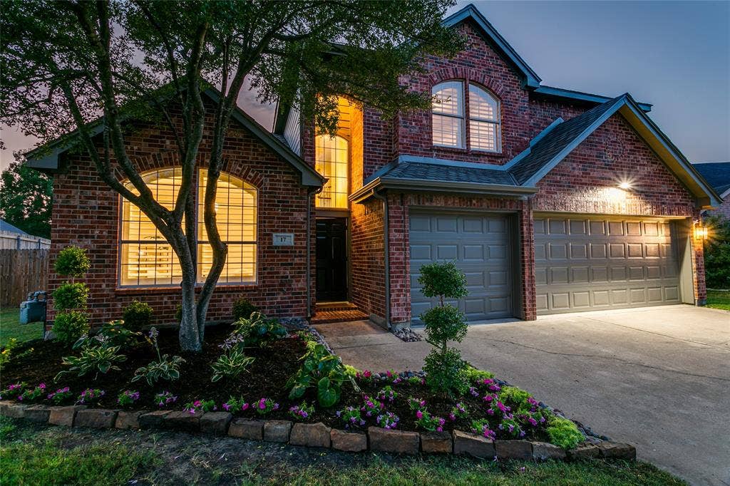 17 Adams Court, Mansfield, TX 76063 Brick exterior with arched windows, an attached Three-car garage, and a landscaped front yard featuring mature trees and planted flower beds
