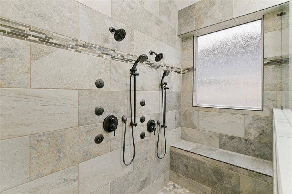 17 Adams Court, Mansfield, TX 76063 Spacious shower with dual shower heads, body sprayers, integrated bench seating, and mixed material tilework including pebble flooring
