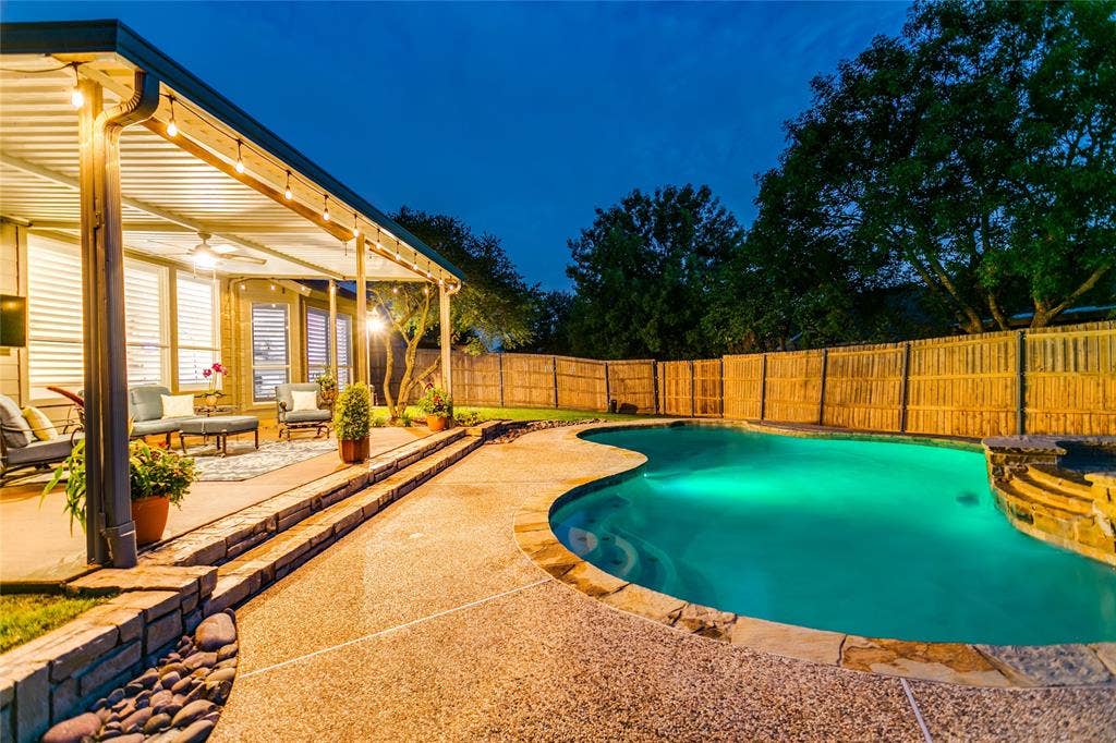 17 Adams Court, Mansfield, TX 76063 Curved spacious swimming pool with integrated stone spa, expansive covered patio with ceiling fan, wood privacy fencing, and stone retaining wall with integrated steps