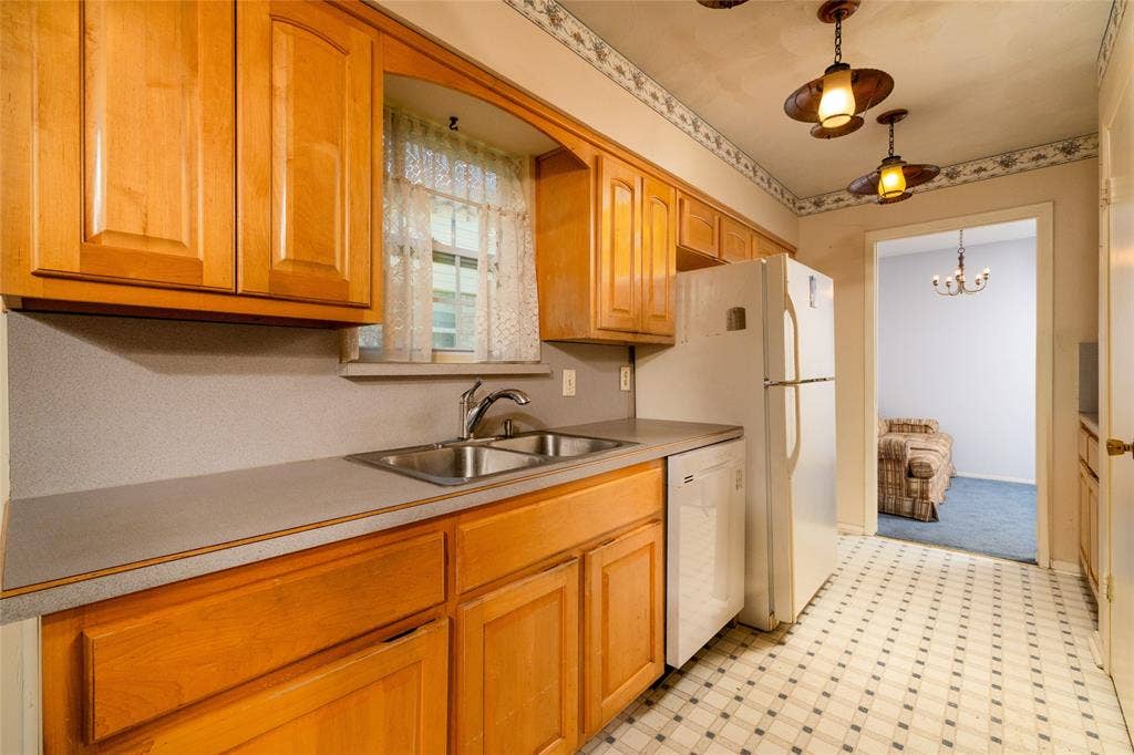 Light-tone wood cabinetry, double basin stainless steel sink, patterned floor tiles, and pendant lighting fixtures