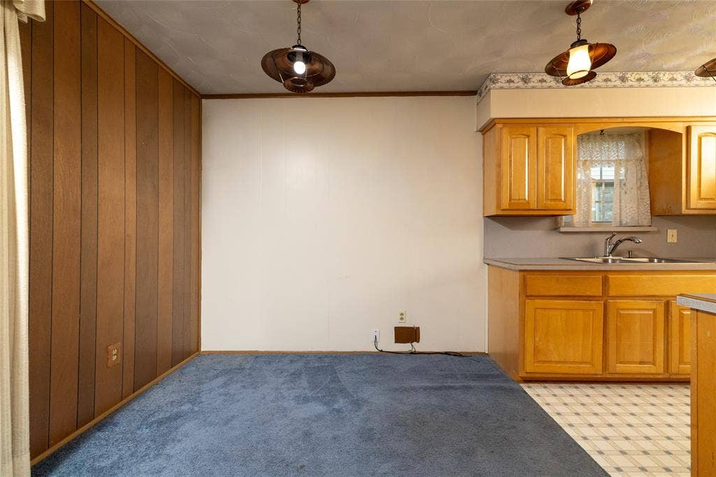 Wood paneling, pendant lighting, light wood cabinetry, laminate countertops, and vinyl tile flooring