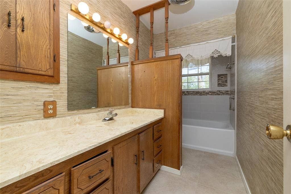 Built-in wooden cabinetry with a light-toned countertop, a full vanity mirror, and a white bathtub with subway tile surround
