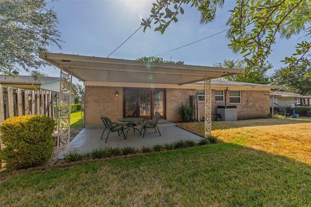 Backyard featuring a covered patio, brick exterior, sliding glass doors, and a manicured lawn