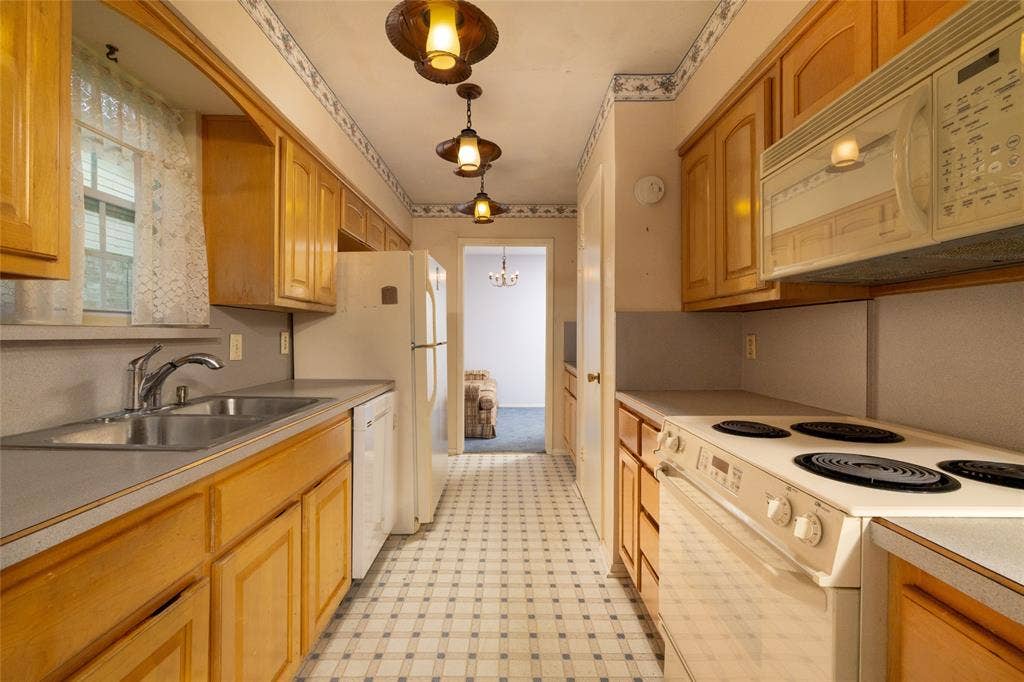 Galley kitchen featuring wood cabinetry, checkerboard flooring, a double basin stainless steel sink, and a built-in microwave
