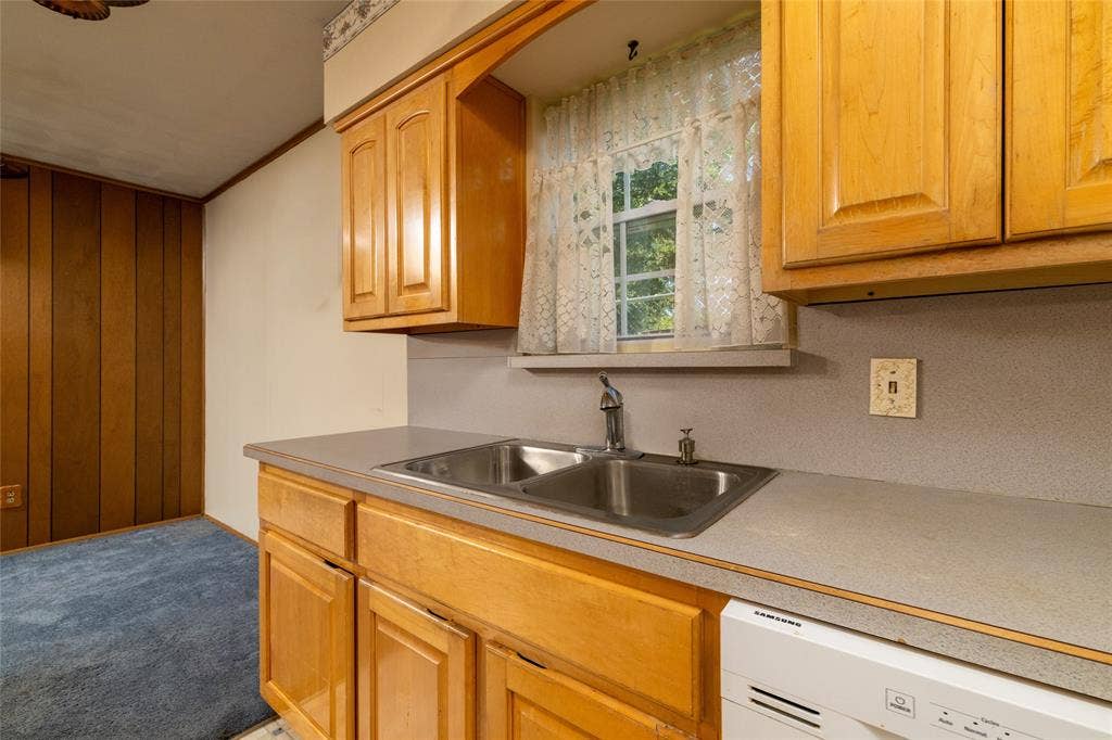 Galley kitchen featuring warm wood cabinetry, stainless steel double-basin sink with chrome faucet, laminate countertops, and white electric range