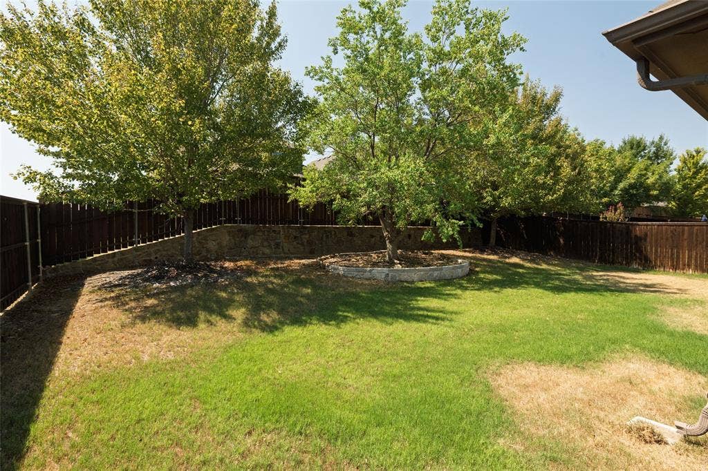 Expansive rear yard featuring green lawn, mature trees, wood privacy fencing, and a stone retaining wall