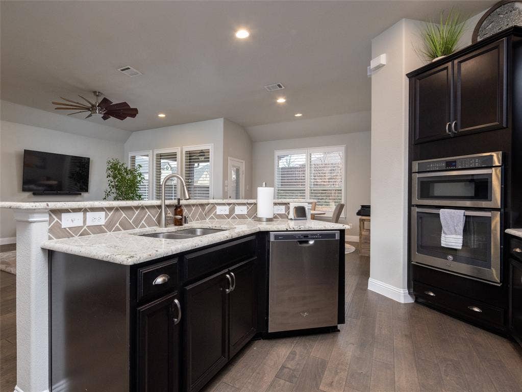 Kitchen featuring dark wood-finish cabinetry, light-toned countertops, stainless steel appliances, and a mosaic tile backsplash