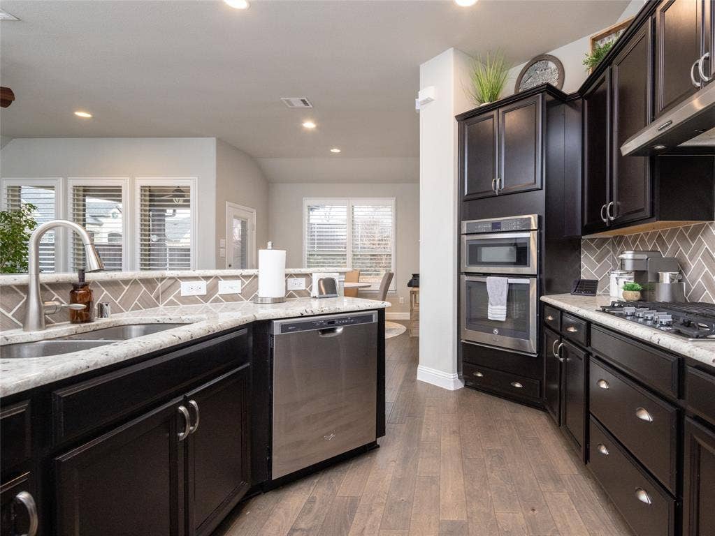 Dark wood-finish cabinetry, stainless steel appliances, granite-style countertops, herringbone tile backsplash, and wood-finish flooring