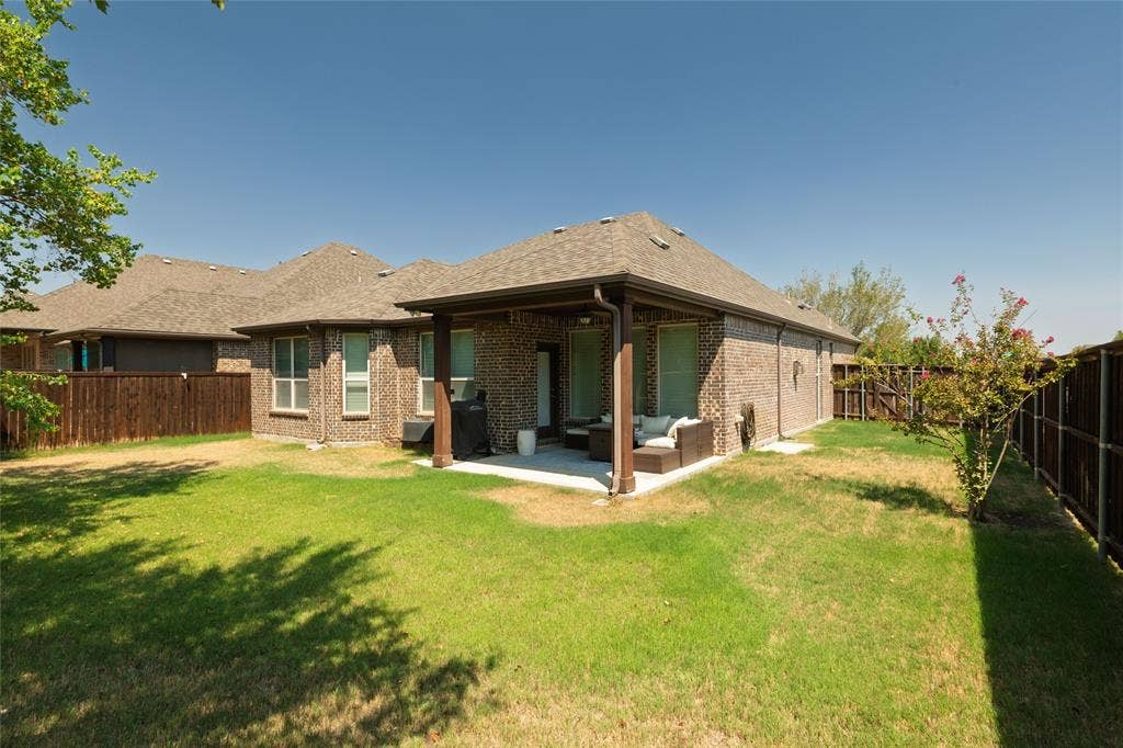 Expansive green lawn featuring a covered patio, brick exterior, and full wood fencing