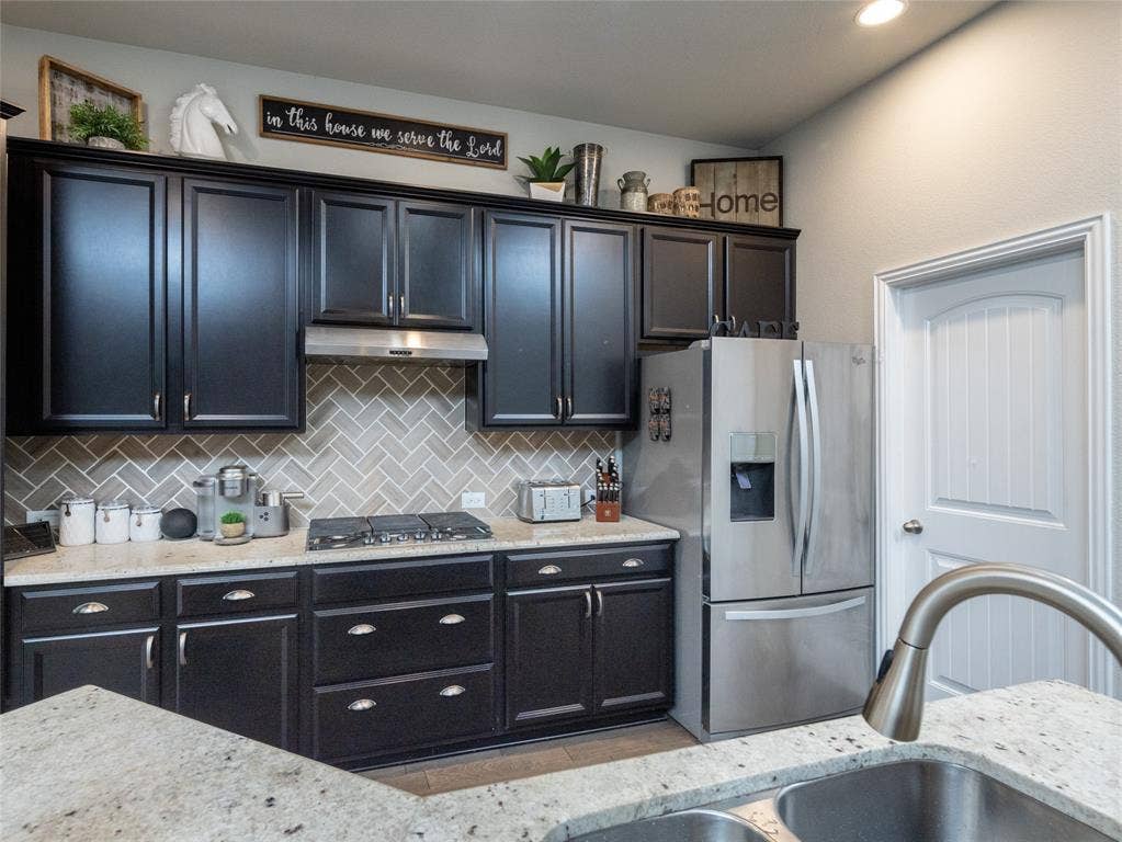 Dark cabinetry with crown molding, stainless steel appliances, herringbone tile backsplash, and light-toned countertops