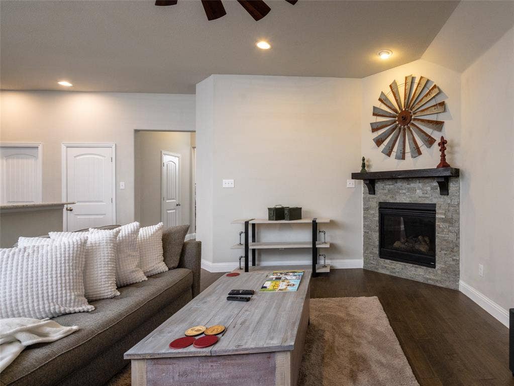 Corner fireplace with stone surround and dark wood mantle, recessed lighting, and wood-finish flooring