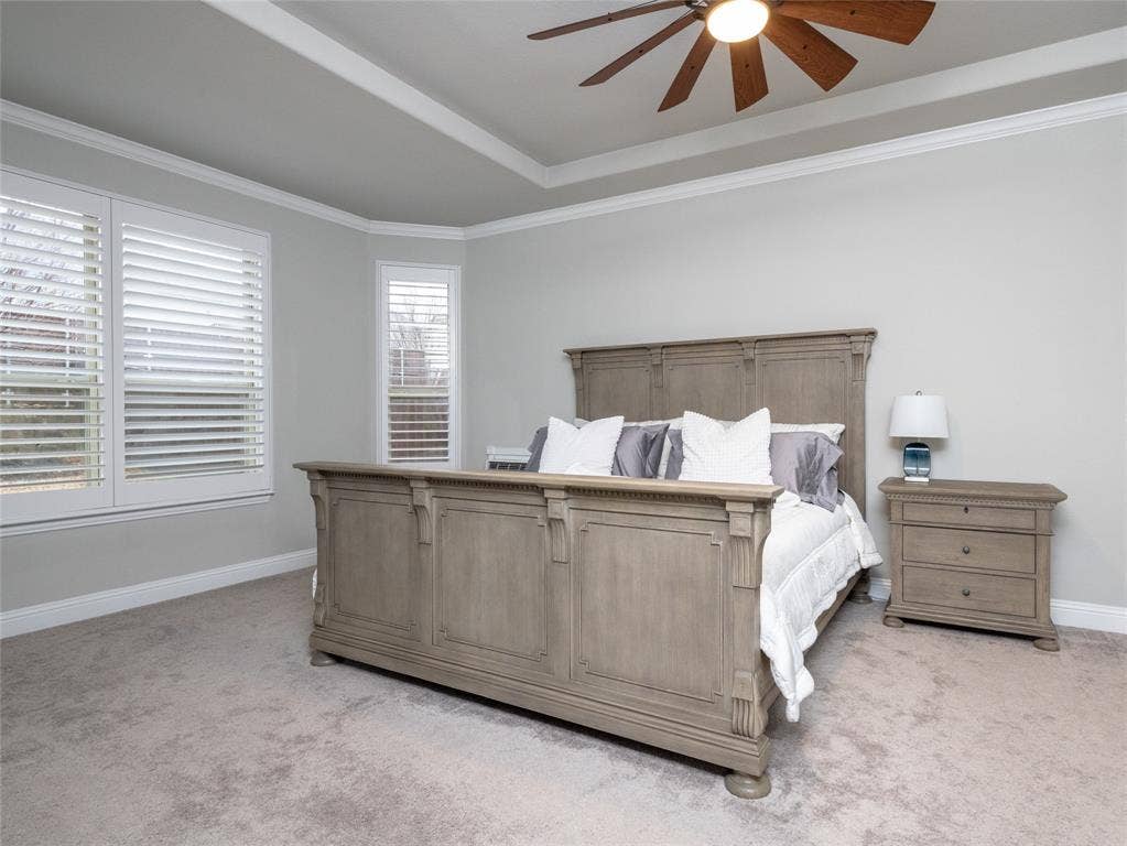 Tray ceiling with crown molding, wood-blade ceiling fan, and light-tone carpeting