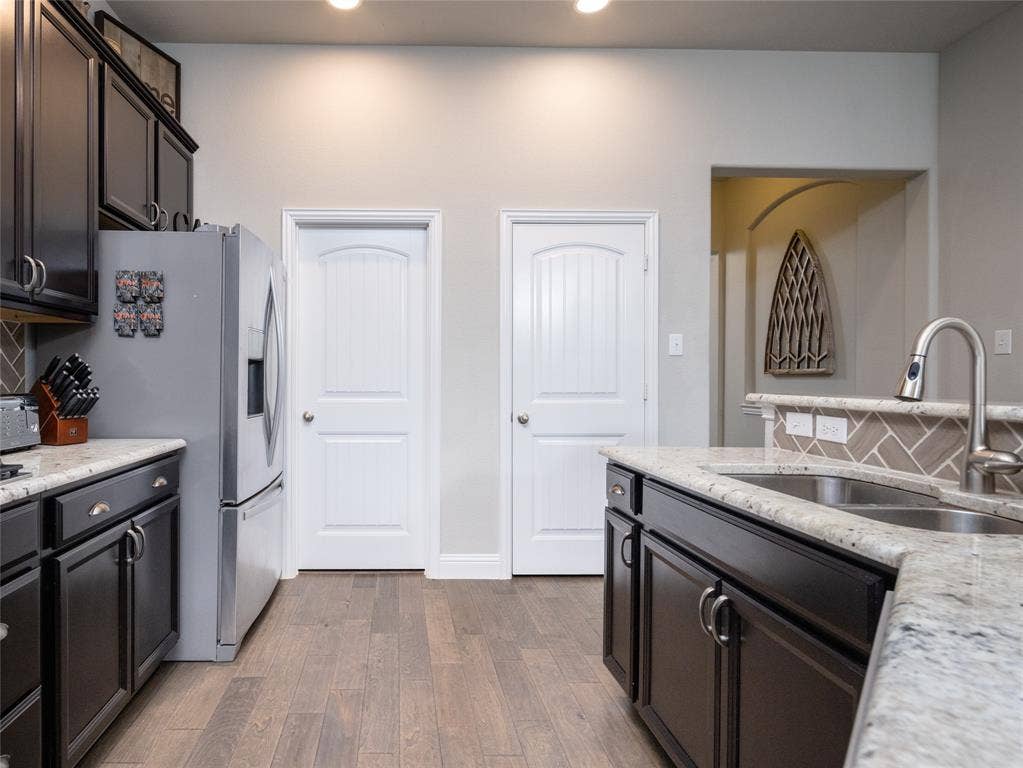Kitchen featuring dark wood-finish cabinetry, light-toned countertops, a stainless steel sink with a pull-down faucet, wood-finish flooring, and a tiled backsplash