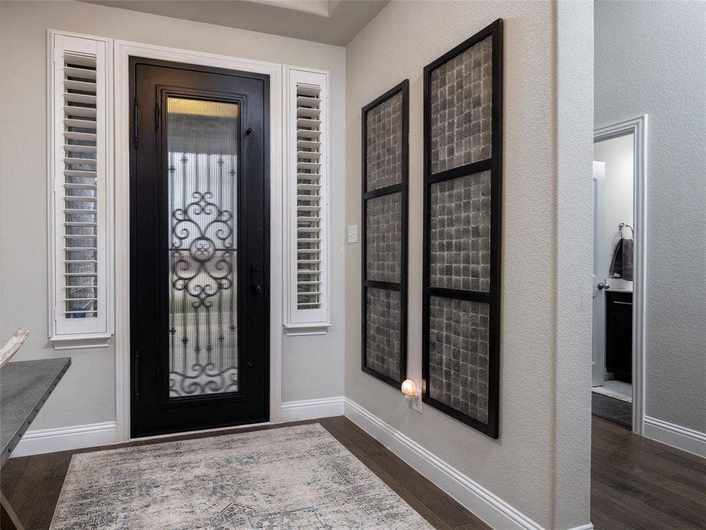 Entryway featuring a black door with decorative ironwork, sidelight windows with plantation shutters, wood-finish flooring, and light gray wall paint