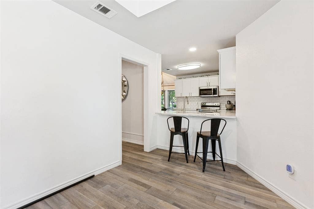 Wood-finish flooring throughout, white baseboards, and a kitchen featuring white cabinetry, a subway tile backsplash, and stainless steel appliances