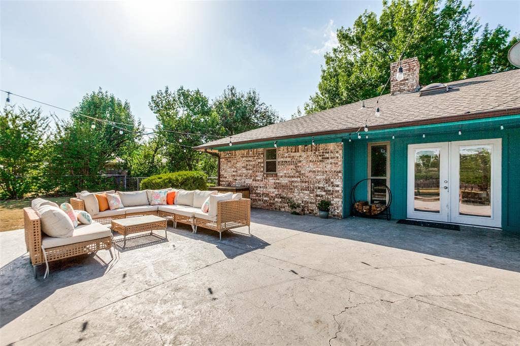 Expansive concrete patio with string lighting, brick exterior, and French doors