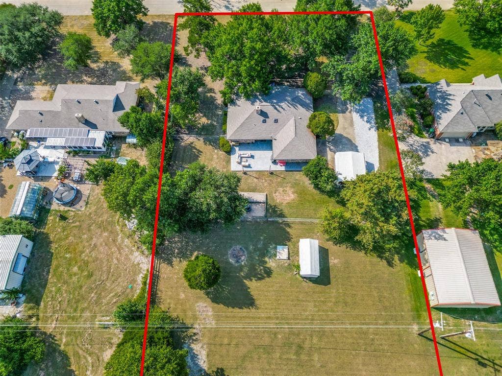 Expansive property featuring a residence with a gray shingle roof, a detached storage building, and mature trees throughout the lot