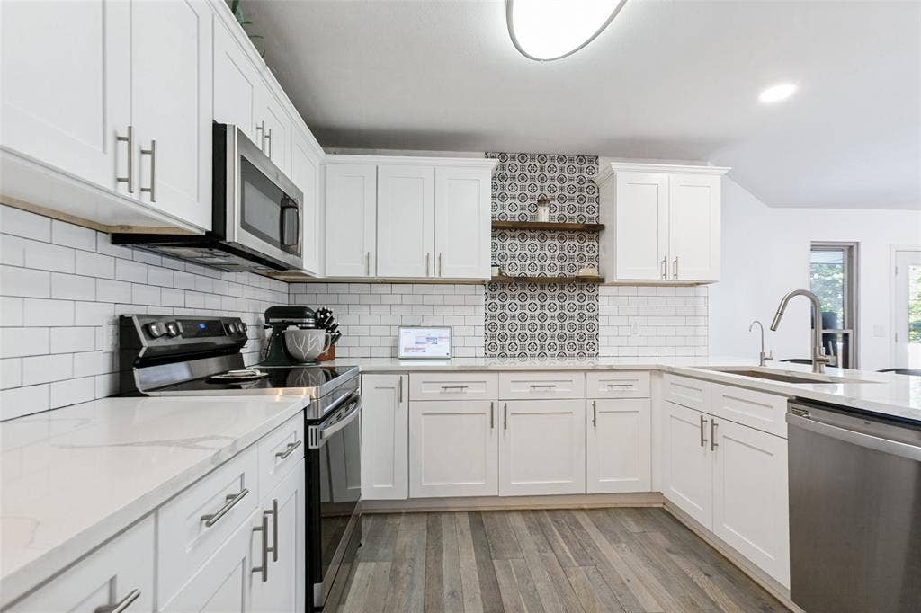 White cabinetry with brushed nickel hardware, light-toned countertops, subway tile backsplash, patterned accent tile, and wood-finish flooring