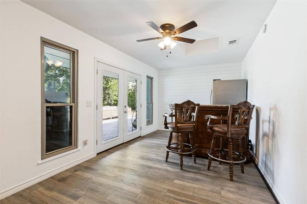 Wood-finish flooring, white shiplap accent wall, ceiling fan with integrated lighting, and double glass doors