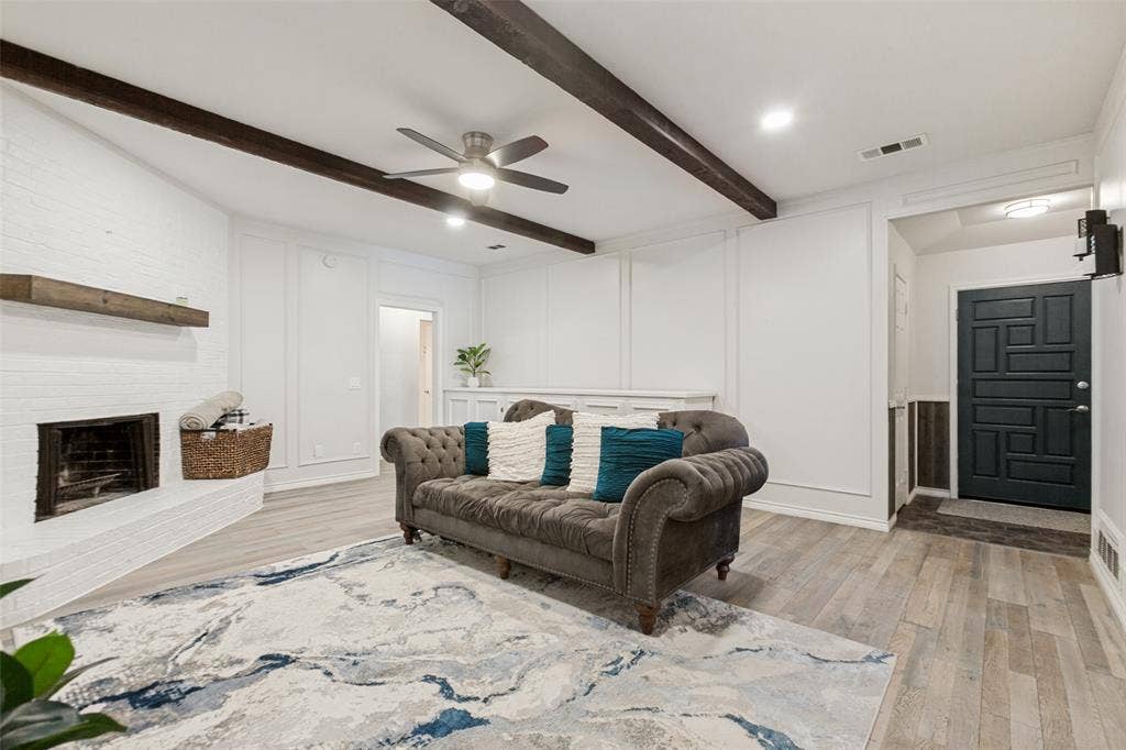 Living area featuring a white brick fireplace, wood-finish flooring, exposed ceiling beams, recessed lighting, and a detailed entry door