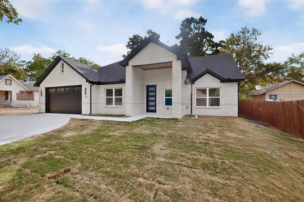 Modern architecture featuring a two-car garage, white brick exterior, black trim, and a contemporary entry door