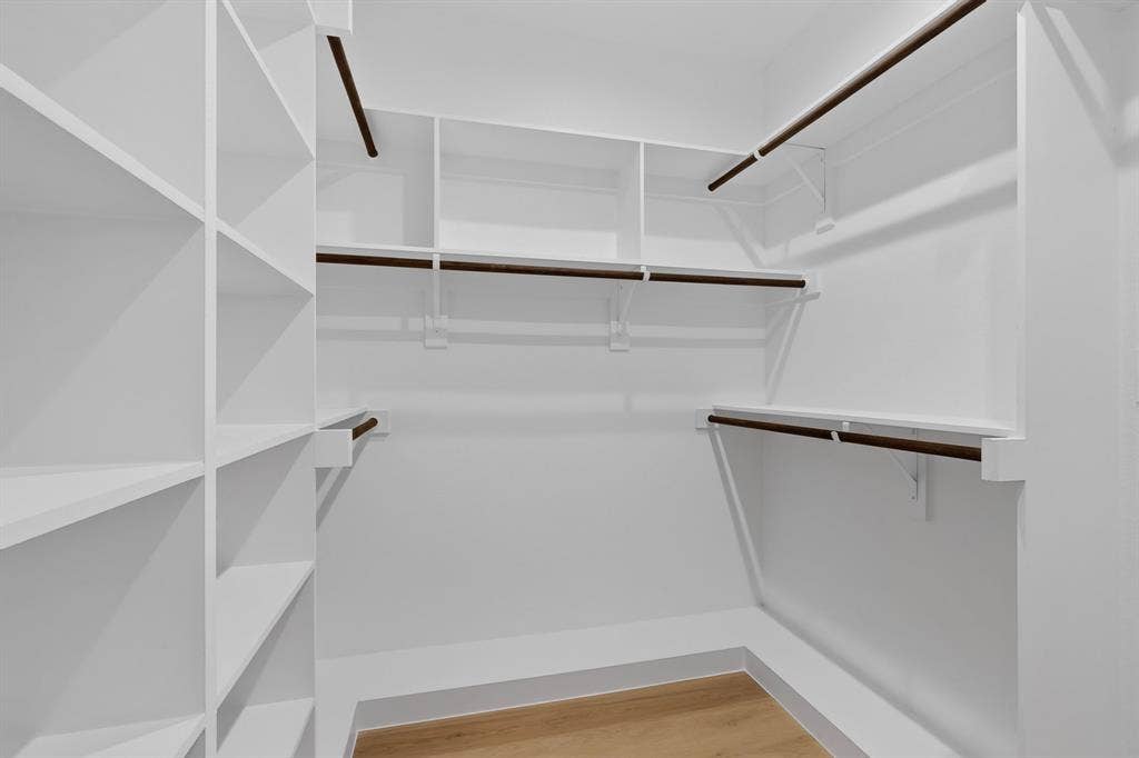 Built-in white shelving, multiple hanging rods, and wood-finish flooring