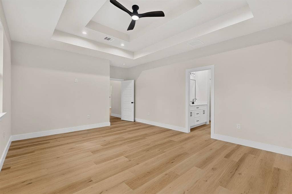 Recessed ceiling with a black ceiling fan, wood-finish flooring, and white interior doors