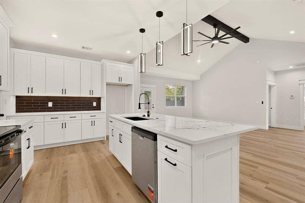 Kitchen featuring white shaker cabinetry, an island with a light-toned countertop, wood-finish flooring, a dark subway tile backsplash, and vaulted ceilings