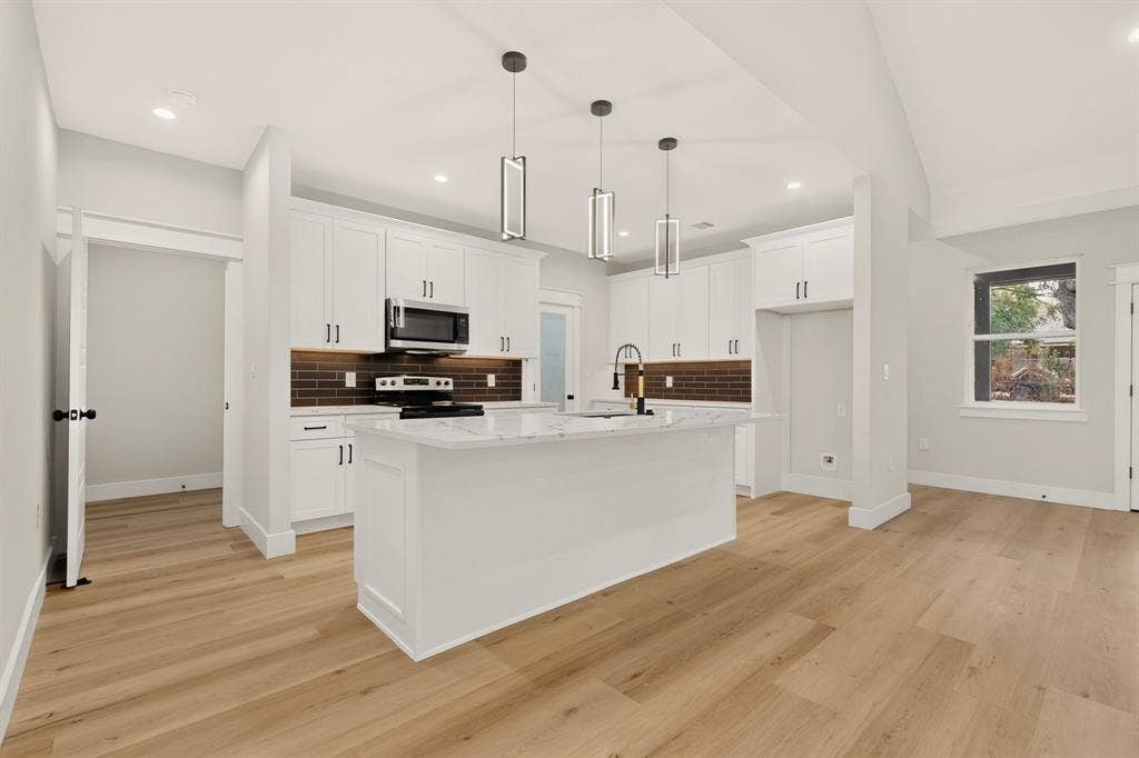 Open-concept kitchen with white cabinetry, a central island with a stone-finish countertop, and wood-finish flooring