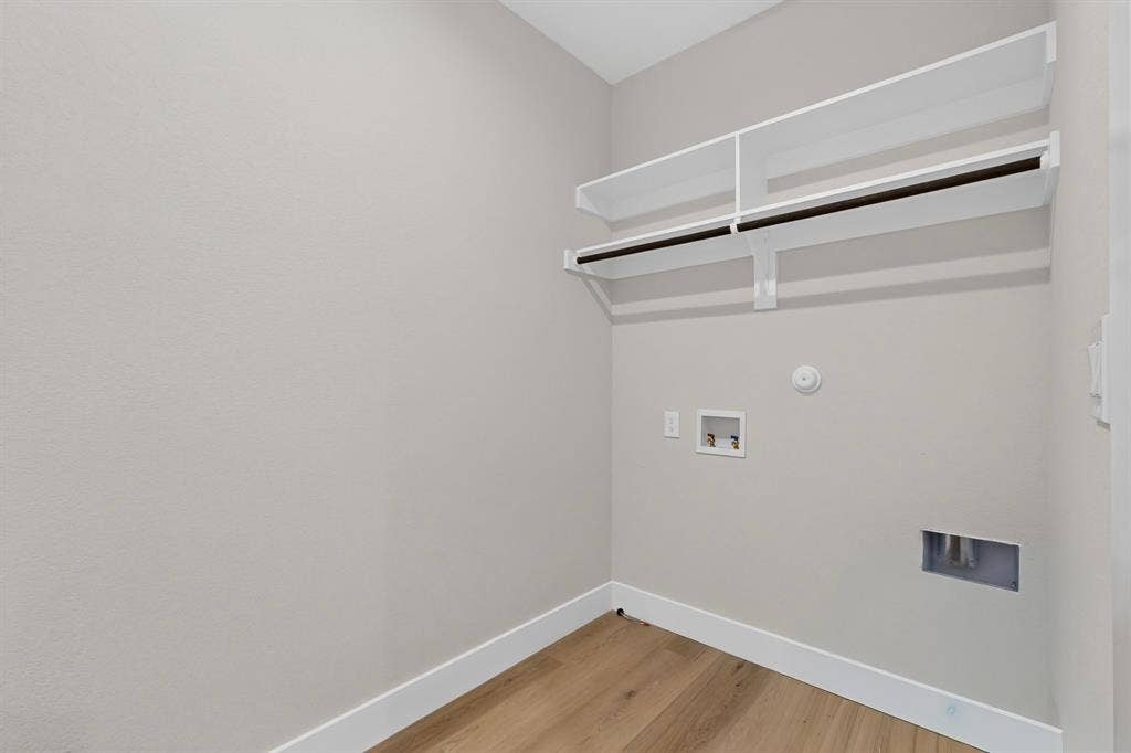 Dedicated laundry area featuring wood-finish flooring, white trim, and built-in shelving with hanging rods