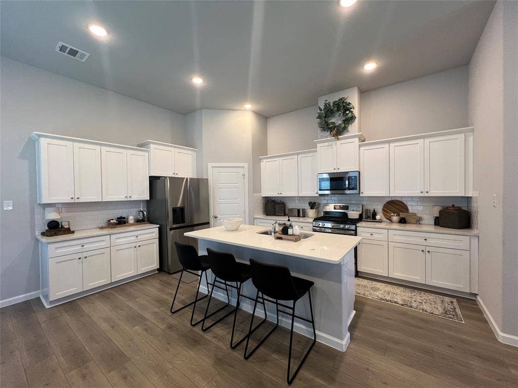 3210 Mattie Grey Lane, Melissa, TX 75454 Kitchen featuring appliances with stainless steel finishes, backsplash, a breakfast bar area, white cabinetry, and dark wood-type flooring
