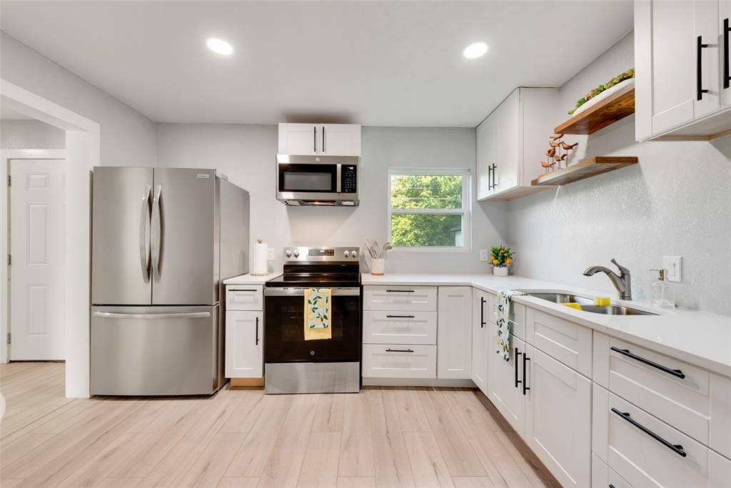 228 Harrison Lane, Hurst, TX 76053 White cabinetry with black hardware, stainless steel appliances, light wood-finish flooring, and a stainless steel sink with a gooseneck faucet