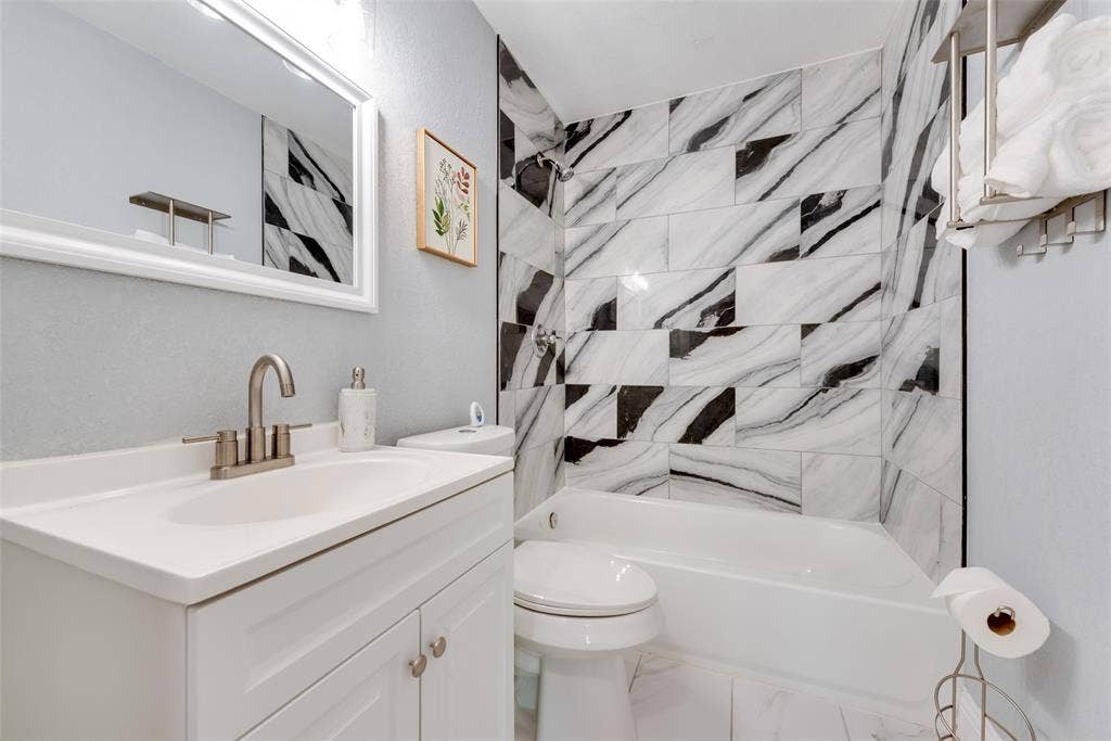 228 Harrison Lane, Hurst, TX 76053 White vanity with integrated sink, brushed nickel faucet, framed mirror, and a tiled shower/tub combination with contrasting black and white patterns