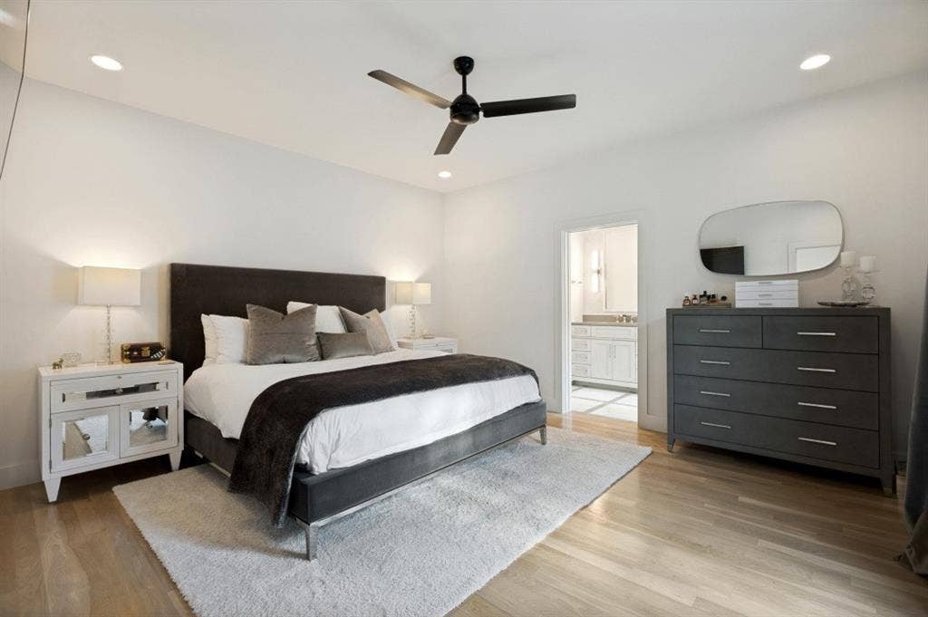 Recessed ceiling lighting, wood-finish flooring, ceiling fan with black blades, white painted walls, and a doorway to an adjoining room with a double vanity