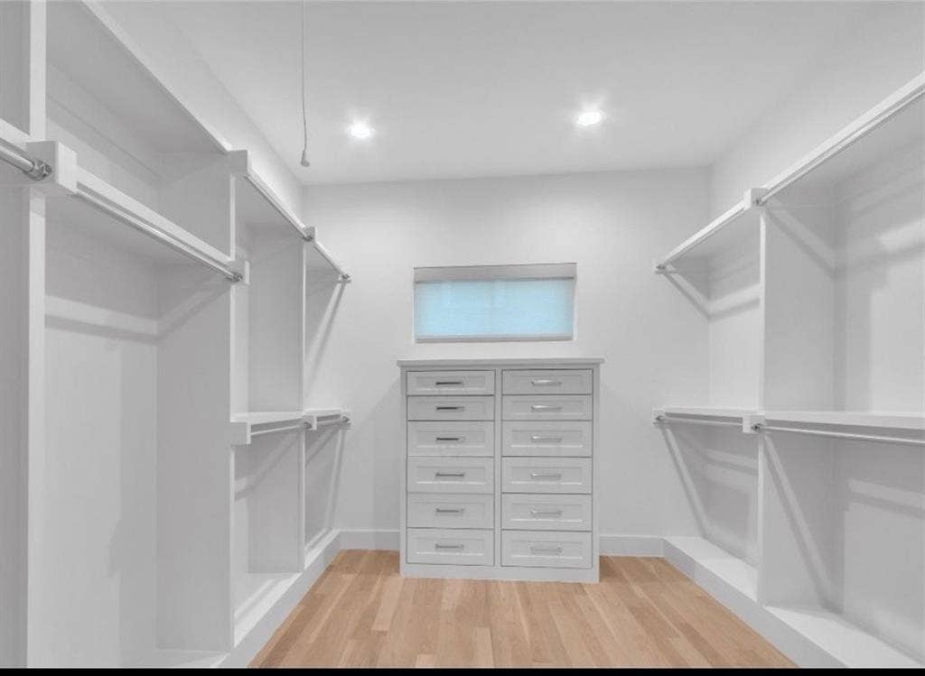 Custom closet system with extensive white shelving, built-in dresser, multiple hanging rods, and wood-finish flooring