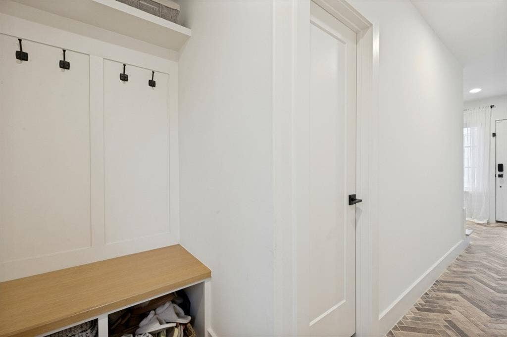 Built-in bench with cubby storage, wall paneling with hooks, and herringbone tile flooring