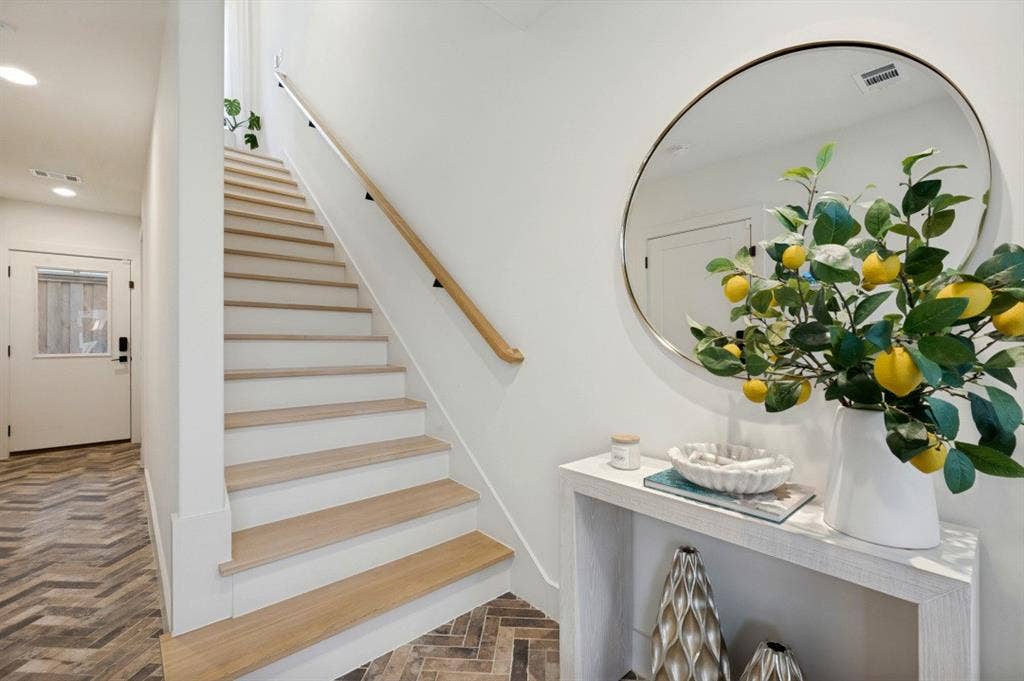 Herringbone wood-finish flooring, staircase with wood treads and white risers, light wood handrail, recessed lighting, and a white entry door with frosted glass insert