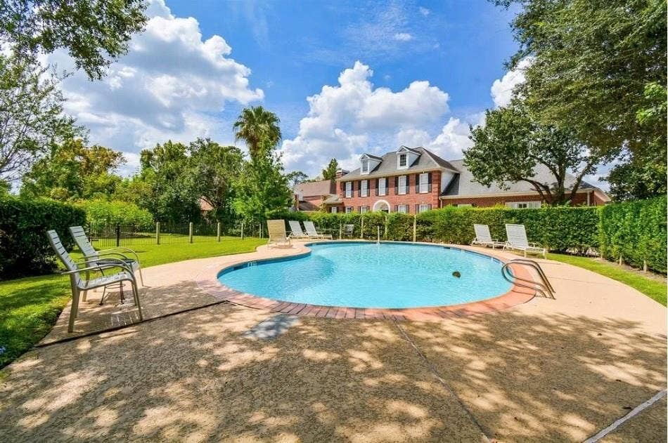 9400 Doliver Drive, #59, Houston, TX 77063 Freeform swimming pool with a surrounding concrete deck, brick coping, and privacy hedging