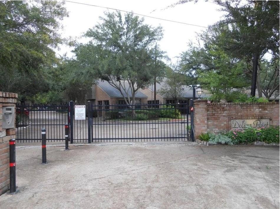 9400 Doliver Drive, #59, Houston, TX 77063 Brick entry column with a built-in mailbox, black metal security gate, brick wall with "Dolphin Point" signage, and established perimeter landscaping