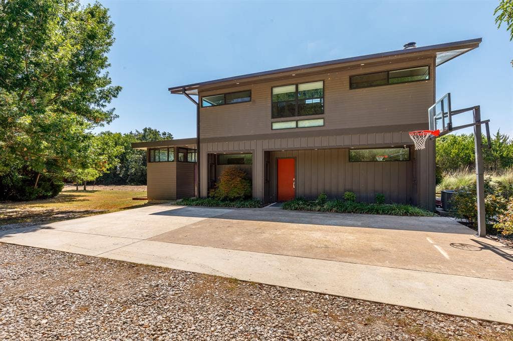 6448 County Road 437, Princeton, TX 75407 Modern two-story exterior with a sloped roofline, a vibrant red entry door, and bastball net on concrete path