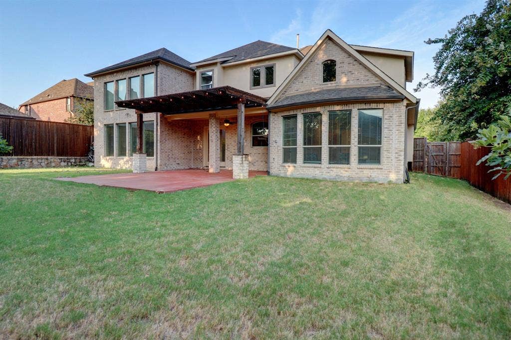 11559 Ashley Lane, Frisco, TX 75035 Brick and stucco exterior with multiple large windows, covered patio, wood pergola, and expansive lawn