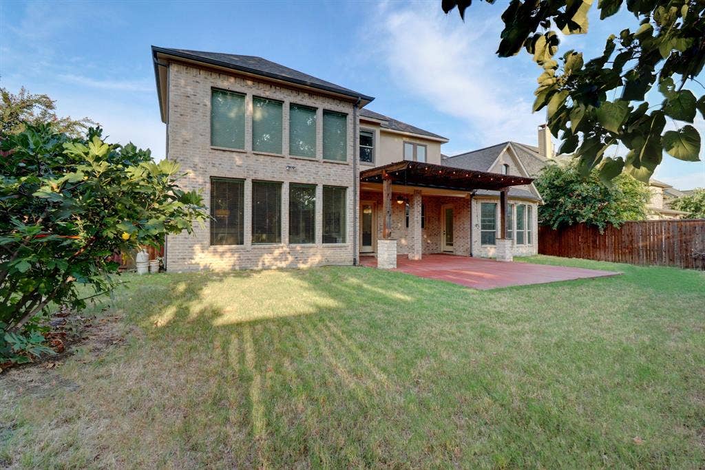 11559 Ashley Lane, Frisco, TX 75035 Expansive backyard featuring a red-toned patio, a pergola with string lights, and a full brick exterior