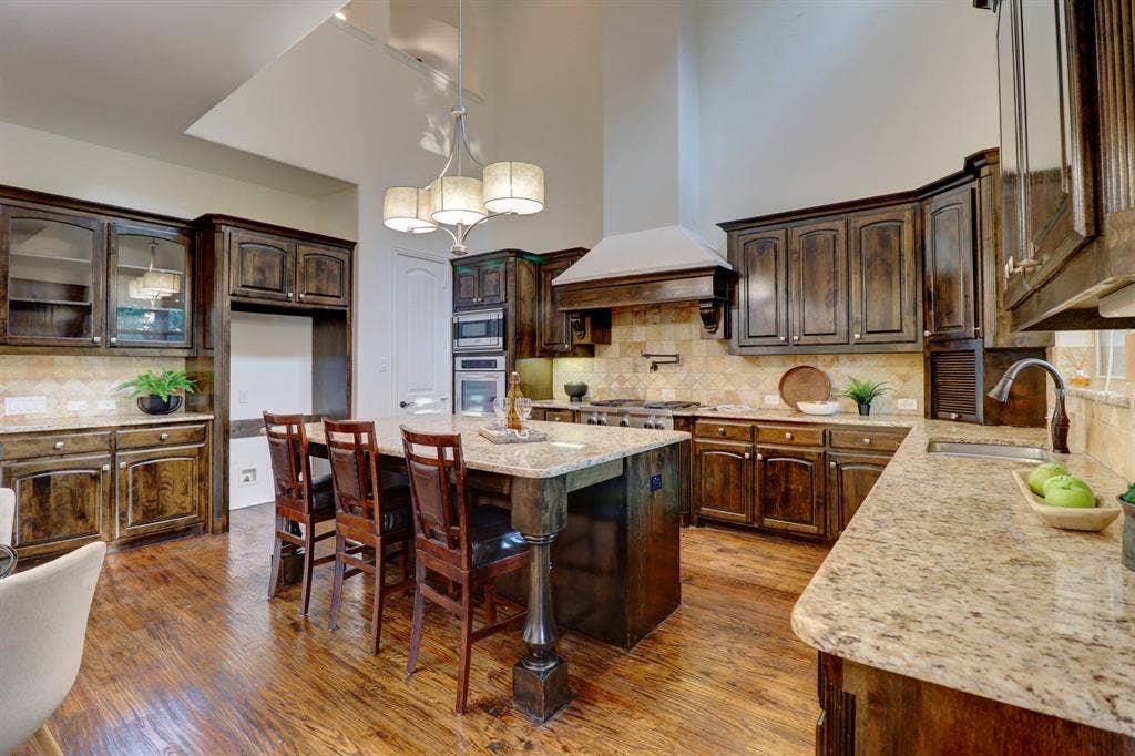 11559 Ashley Lane, Frisco, TX 75035 Spacious kitchen featuring rich wood cabinetry, granite countertops, wood-finish flooring, a central island with seating, and stainless steel appliances