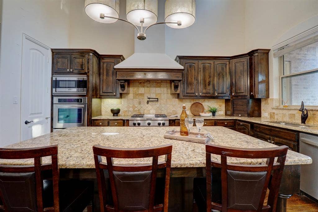 11559 Ashley Lane, Frisco, TX 75035 Kitchen featuring a granite island, coordinating countertops, dark wood cabinetry, stainless steel appliances, and a tile backsplash