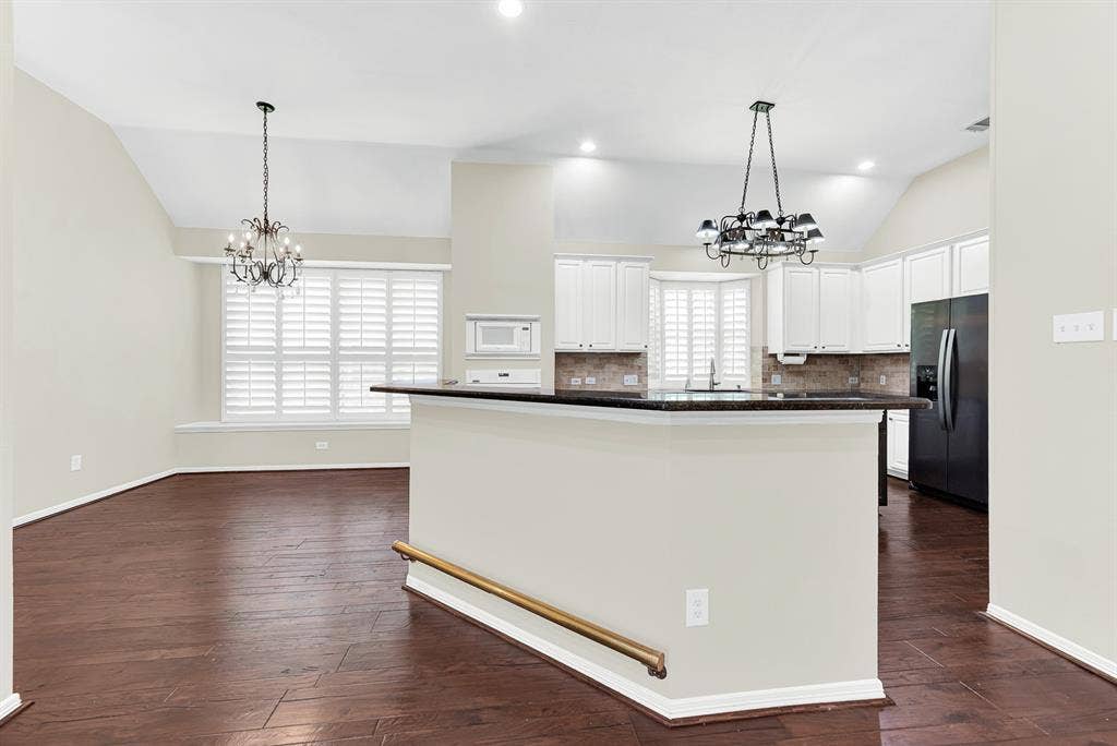 3217 Royal Melbourne Drive, Plano, TX 75093 A raised breakfast bar with dark granite counters sets the stage for this open kitchen, anchored by double chandeliers and high vaulted ceilings. It creates an easy, inviting flow where guests can gather for drinks while you finish prepping dinner.