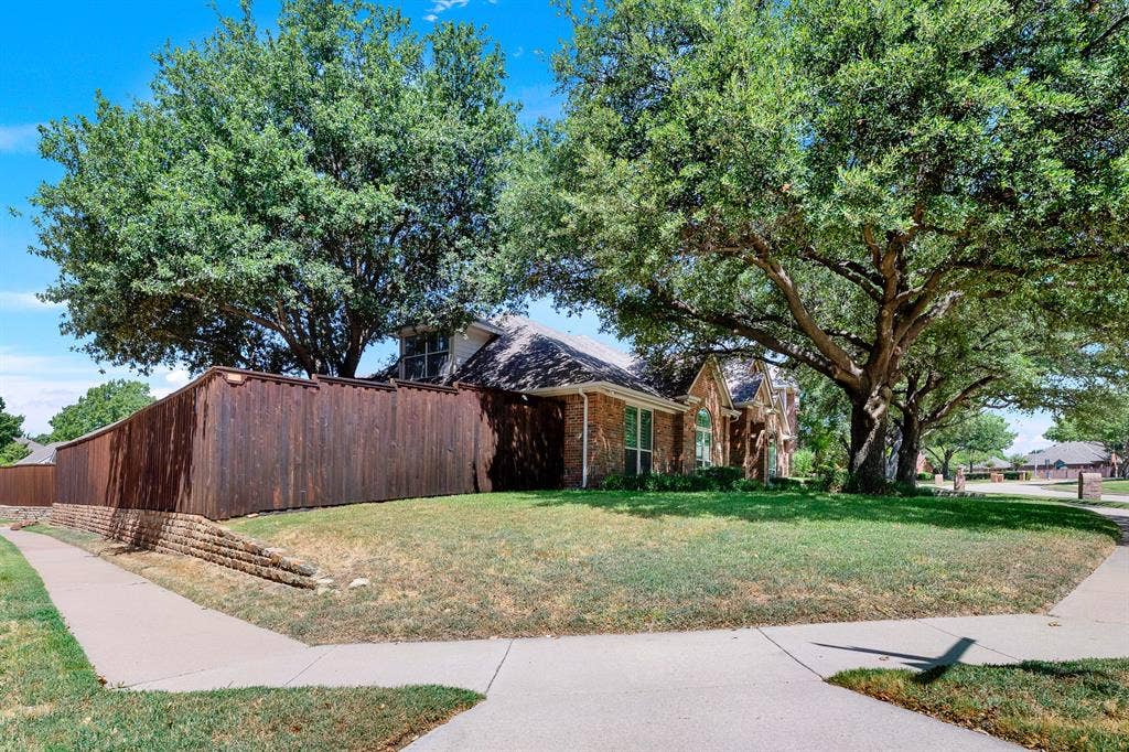 3217 Royal Melbourne Drive, Plano, TX 75093 A sweeping view of the side lawn showcases a impressive shade tree framing the back brick elevation and private garden area. This extra green space on the corner lot gives you room to relax outdoors, tend to your garden, or simply enjoy quiet mornings under the trees.